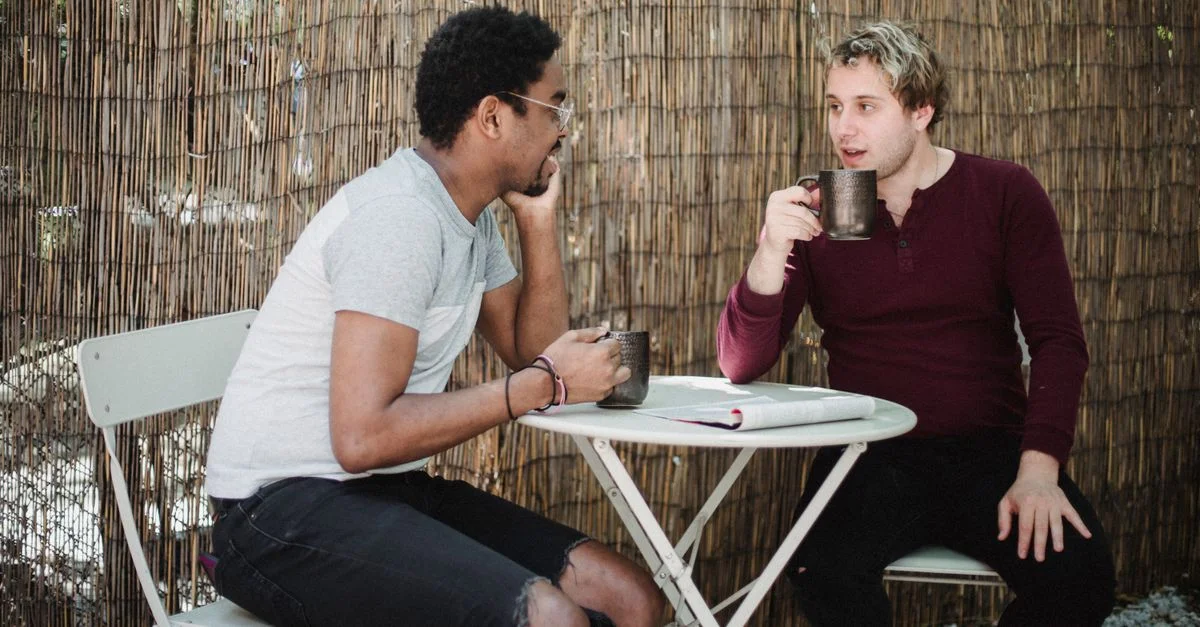 Deux hommes profitent d'une conversation décontractée autour d'un café en extérieur avec un fond rustique.
